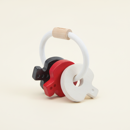 PlanToys wooden baby key rattle in black, white and red with a cord ring and wooden bead on a plain cream background