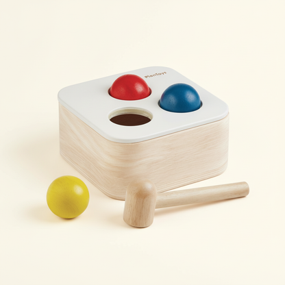 PlanToys wooden punch-and-drop bin with fabric top and three wooden balls on a plain cream background